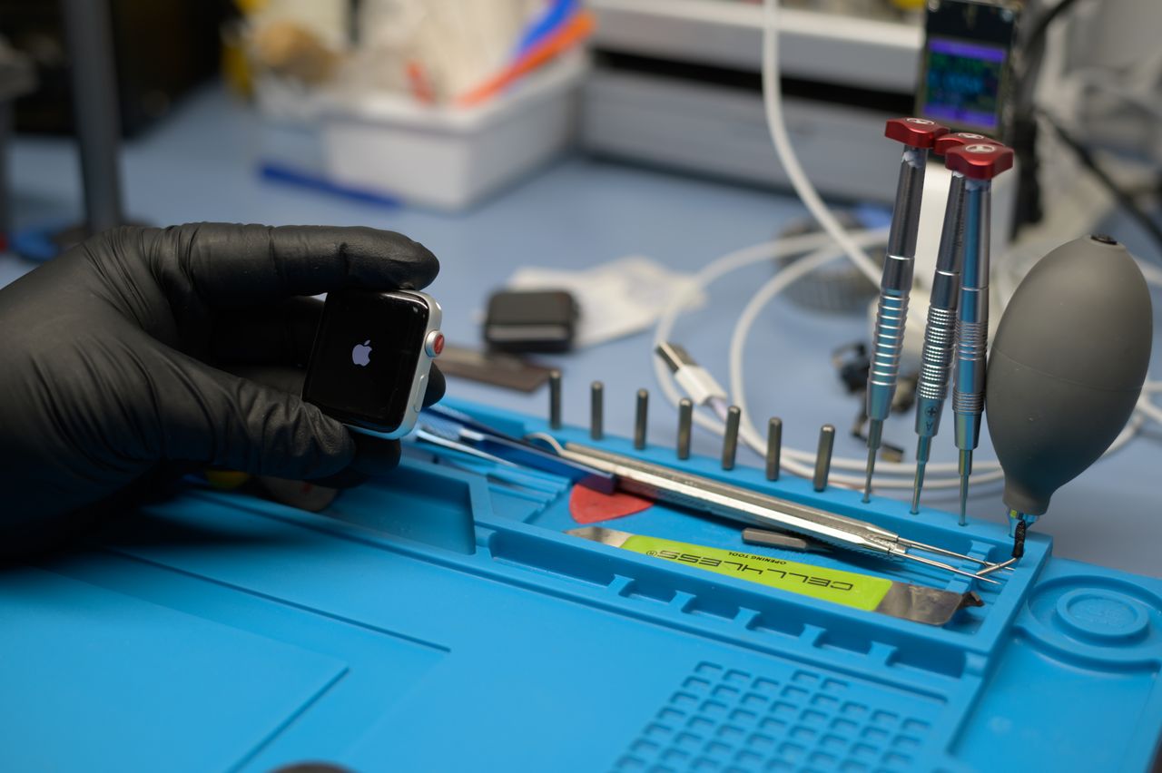 Technician in black gloves repairing a smartwatch with precision tools and equipment.